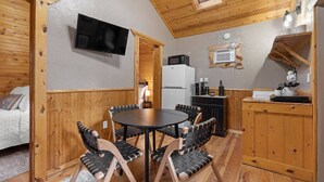 A cozy room with a round table and chairs, a television mounted on the wall, a kitchen area with a refrigerator and microwave, and a wooden ceiling with a skylight. - Angler’s Haven Cabin: Black Hills Quiet Escape (Rapid City)