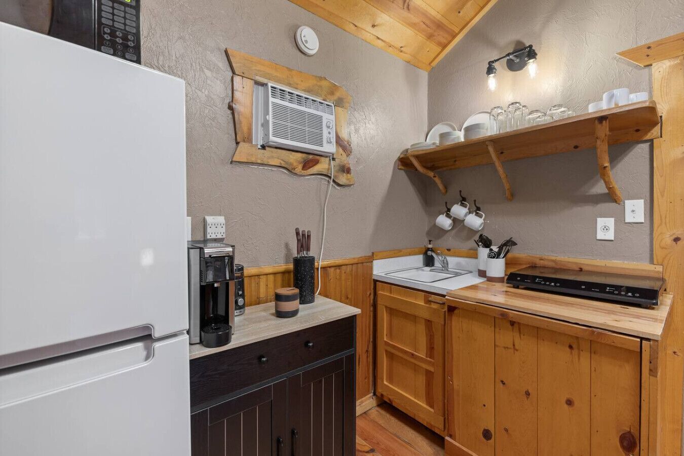 Eine kompakte Küche mit Holzausbau, einer integrierten Mikrowelle, einer Kaffeemaschine und einem Regal mit Küchenutensilien.