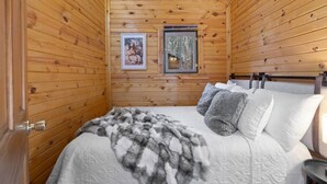 A cozy wooden cabin bedroom with a bed, pillows, a blanket, and a framed picture on the wall. - Angler’s Haven Cabin: Black Hills Quiet Escape (Rapid City)