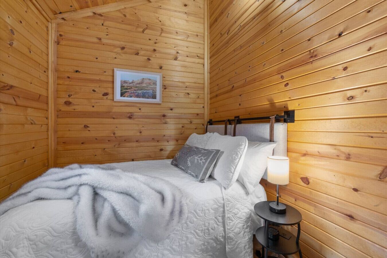 Een knus houten vertrek met een bed, een nachtkastje en een ingelijste foto aan de muur.