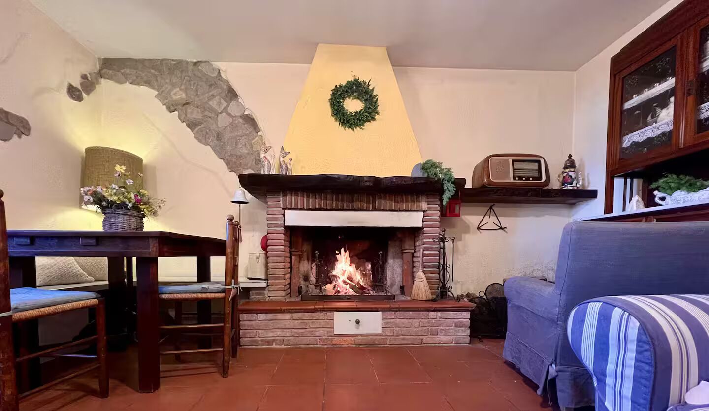 A cozy living room with a fireplace, a stone wall, a blue sofa, and a wooden table with chairs.