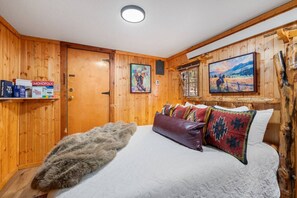 A wooden-paneled room with a bed, a fur throw, and two paintings on the wall. - Timber Ridge Cabin: Rustic Getaway (Rapid City)