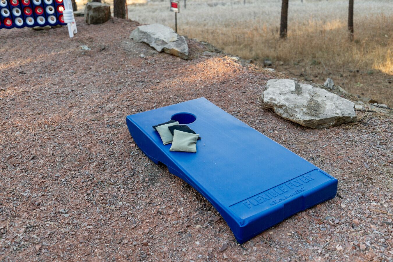 A blue disc golf basket with a net and two discs on top, set on a gravel surface with rocks and a flag in the background.