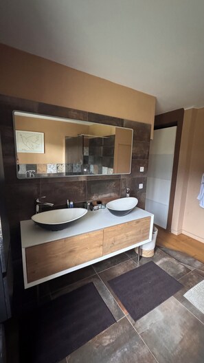 A modern bathroom with two sinks, a large mirror, and a wooden vanity.