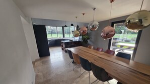 A modern dining area with a long wooden table, black chairs, and a view of the outdoors through large windows. - Charming Provencal villa with pool Cabriès (Cabriès)