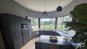 A modern kitchen with a curved island, dark cabinetry, and large windows offering a view of the outdoors. - Charming Provencal villa with pool Cabriès (Cabriès)