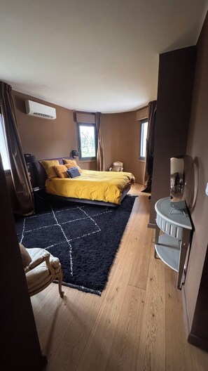 A bedroom with a bed, a small bedside table, a chair, a mirror, and a window.