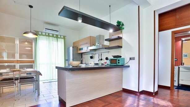 Una cucina moderna con isola centrale, illuminazione a sospensione e pavimento con motivo a spina di pesce.