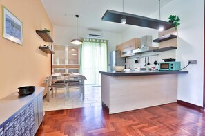 A modern kitchen with a central island, wooden cabinets, and a dining area with a glass table. - GuestHost - A cozy and spacious 83 square meters apartment, perfect for four people, located on the fourth floor of a building with an elevator (NOT accessible to guests with disabilities).The property enjoys an excellent seafront location: our guests ca (Pozzuoli)
