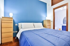 A bedroom with a blue wall, a bed with white and blue bedding, wooden nightstands, and a wooden dresser. - GuestHost - A cozy and spacious 83 square meters apartment, perfect for four people, located on the fourth floor of a building with an elevator (NOT accessible to guests with disabilities).The property enjoys an excellent seafront location: our guests ca (Pozzuoli)