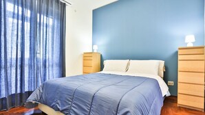 Una camera da letto con un letto, comodini in legno, una parete blu e una finestra con tende.