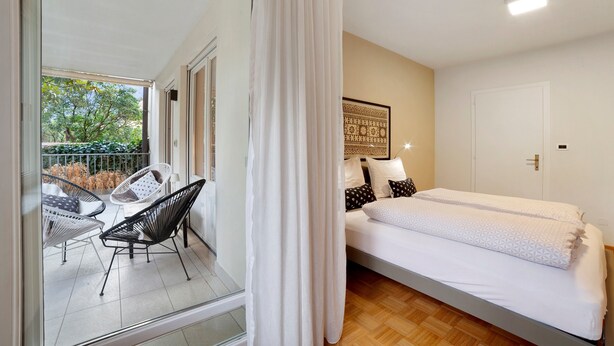 Une chambre à coucher avec un lit, une fenêtre avec des rideaux, une chaise et une œuvre d’art accrochée au mur.