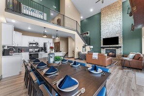 A spacious dining area with a long table set for six, a kitchen with modern appliances, a fireplace, and a balcony with a view. - Luxury Lakeview Cabin + Lazy River & Pickleball (Kimberling City)