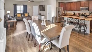 Een ruime woonkamer met een grote houten eettafel, een keuken met donker houten kasten en een zithoek met een bank en stoelen.