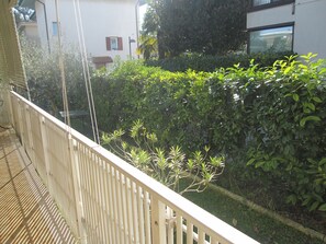 Un balcón con baranda blanca que da a un jardín con diversas plantas y un edificio blanco al fondo.