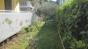 Un jardin avec un pot de fleurs, une table en métal et une zone herbeuse.