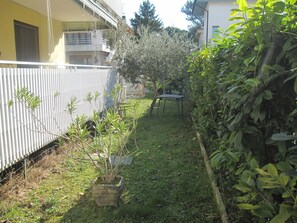 A garden with a potted plant, a metal table, and a grassy area. - Cozy Flat With Garden Near Beach (Grado)