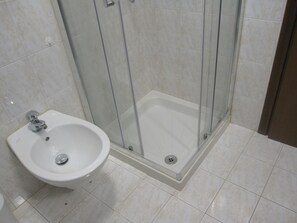 Ein Badezimmer mit einer Duschkabine aus Glas, einem weißen Waschbecken auf Säule und gefliestem Boden.