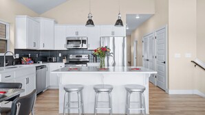 A modern kitchen with white cabinets, stainless steel appliances, and a central island with stools. - Luxury Cabin Private Hot Tub and Steps to Pools! (Kimberling City)