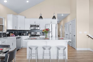 A modern kitchen with white cabinets, stainless steel appliances, and a central island with stools. - Luxury Cabin Private Hot Tub and Steps to Pools! (Kimberling City)