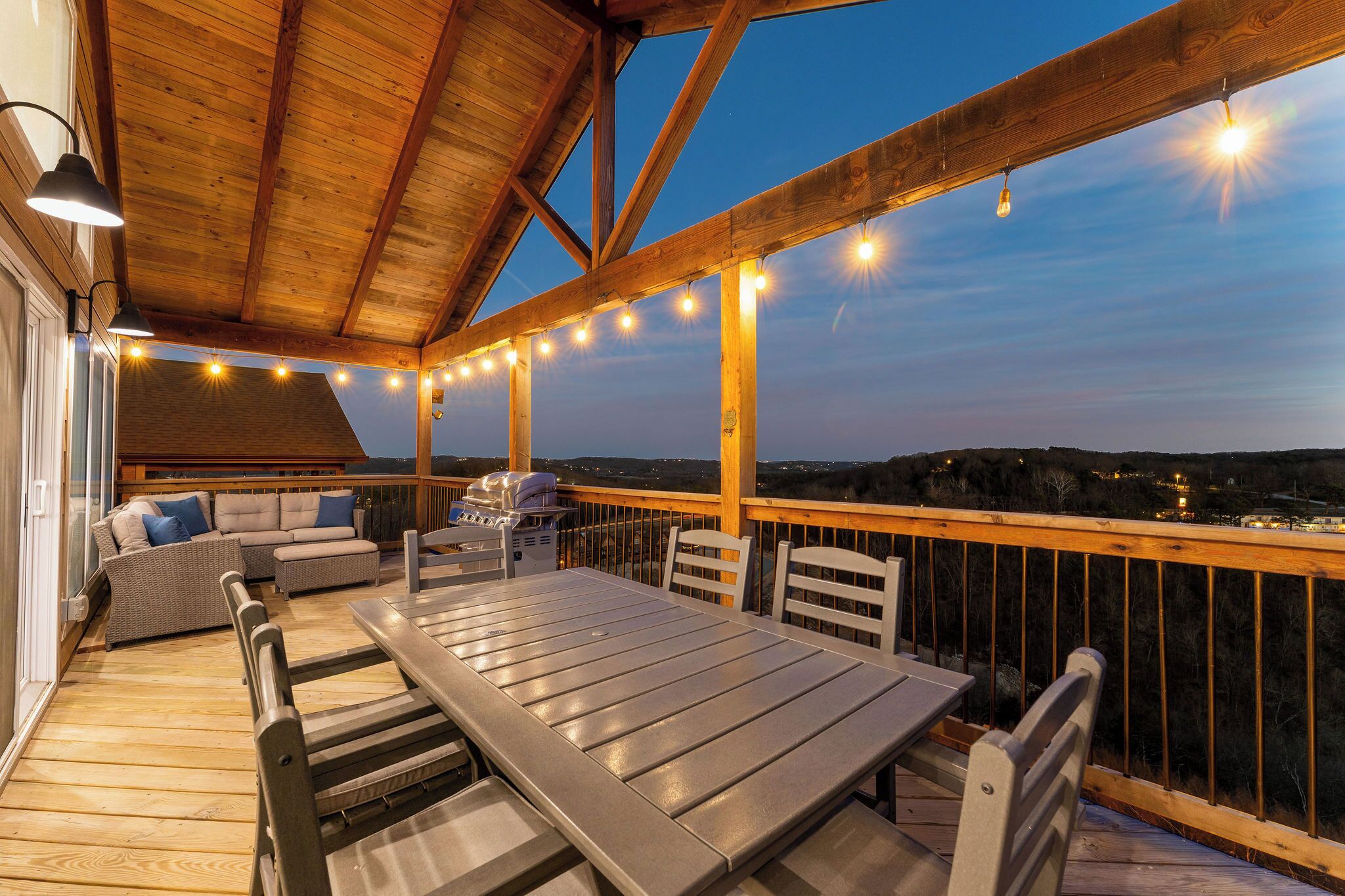 Une terrasse extérieure dotée d’un plafond en bois, de guirlandes lumineuses, d’une table à manger, de chaises et d’un canapé.