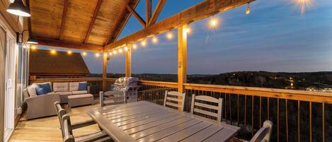 Une terrasse extérieure dotée d’un plafond en bois, de guirlandes lumineuses, d’une table à manger, de chaises et d’un canapé.