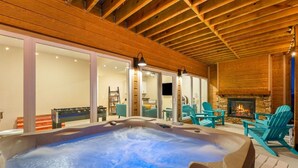 A hot tub with a stone fireplace, wooden ceiling beams, and teal chairs. - Luxury Cabin Private Hot Tub and Steps to Pools! (Kimberling City)