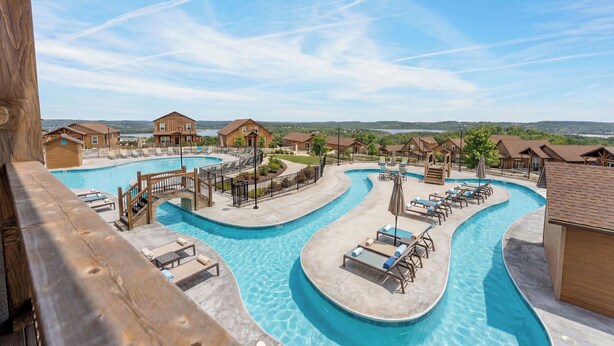 Ein Resort mit großzügiger Poolanlage, Holzhäusern und einem malerischen Hügelblick.