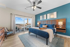 Une chambre à coucher avec un lit, une table de chevet, un ventilateur de plafond, une vue sur le balcon et une grande fenêtre.