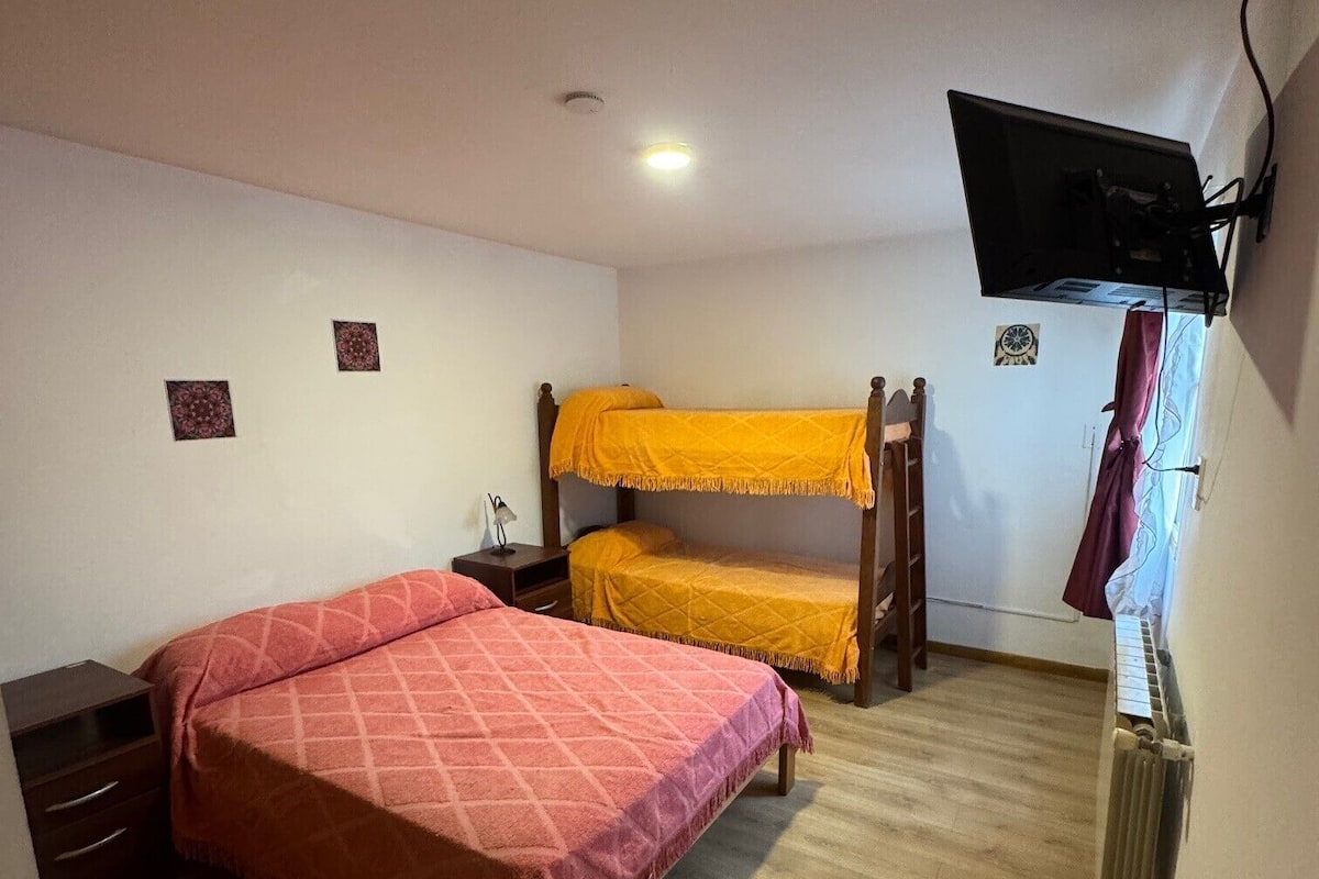 Een slaapkamer met een stapelbed, een enkel bed, een bureau, een stoel, een aan de muur bevestigde televisie en een radiator.