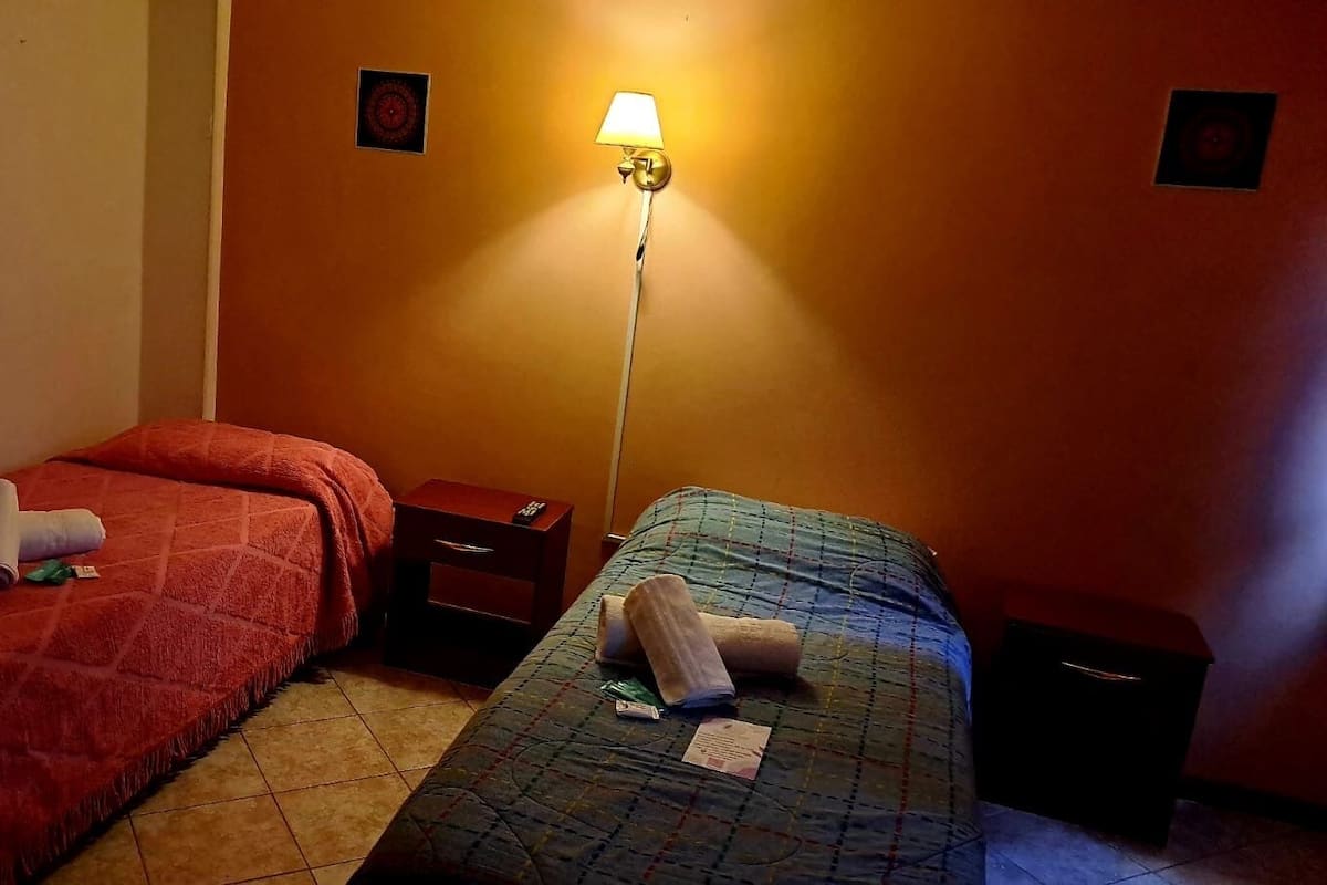 Een hotelkamer met twee bedden, elk met een andere kleuren dekbedovertrek, een nachtkastje, een lamp en een kleine wanddecoratie.