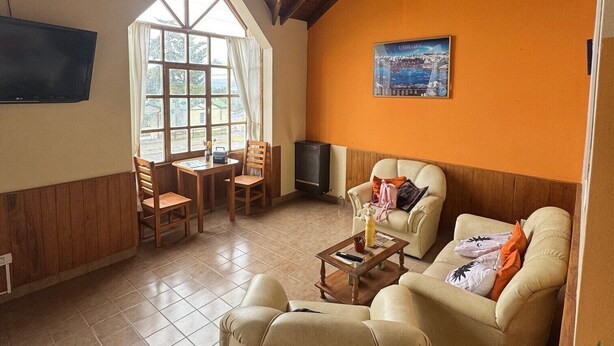 A cozy living room with wooden beams, a fireplace, a television, and a large window. - HOSTERIA  AILEN (Ushuaia)