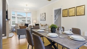 Un comedor con una mesa larga dispuesta para cuatro personas, rodeada de sillas. Hay una planta en maceta sobre la mesa, y la habitación tiene un diseño moderno con una araña.