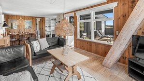 A modern living room with a wooden interior, a dining area, and a large window offering a view of the outdoors. - "Monna" -  from the sea by Interhome (Hvide Sande)