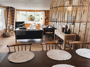 A cozy cabin interior with a wooden interior, a sofa, a dining table with placemats, a TV, and a large window. - "Monna" -  from the sea by Interhome (Hvide Sande)