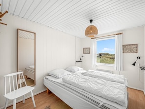 A bedroom with a bed, a chair, a window with a view, and a hanging light fixture. - "Monna" -  from the sea by Interhome (Hvide Sande)