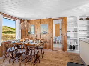 A dining area with a wooden table set for six, wooden chairs, a hanging light fixture, and a view of the outdoors. - "Monna" -  from the sea by Interhome (Hvide Sande)