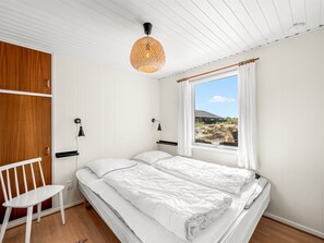 A bedroom with a bed, a chair, a window with curtains, and a hanging light fixture. - "Monna" -  from the sea by Interhome (Hvide Sande)