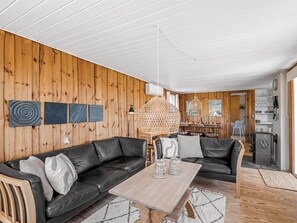 Een gezellige woonkamer met een houten wand, een zwarte leren bank, een houten salontafel en een hanglamp.