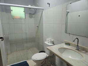 Een badkamer met douche, toilet, wastafel en spiegel.