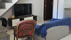 Ein Wohnzimmer mit Fernseher, einem Korbstuhl, einer Couch und einer Treppe.