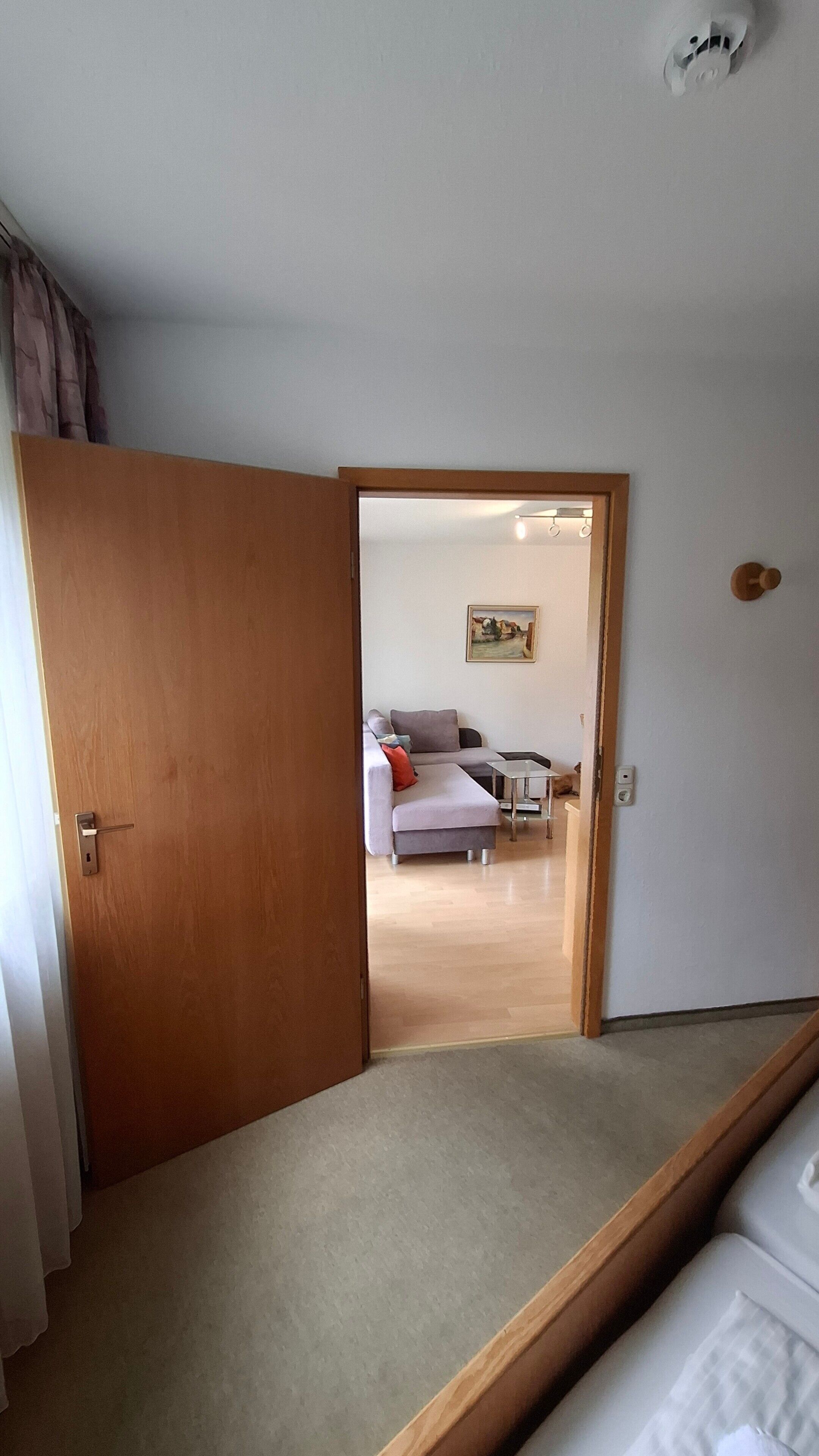 Ein Zimmer mit Holztür, grauem Sofa, kleinem Tisch und einem Gemälde an der Wand.