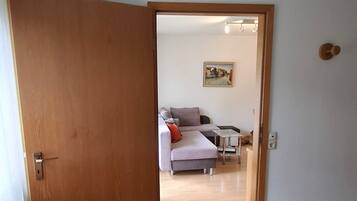 Ein Zimmer mit Holztür, grauem Sofa, kleinem Tisch und einem Gemälde an der Wand.