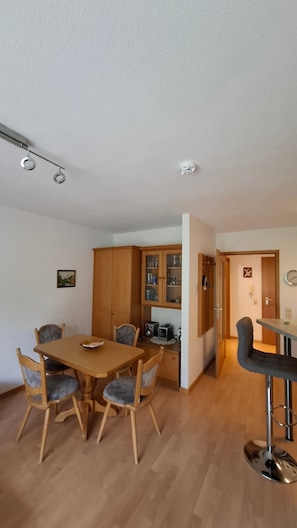Ein Essbereich mit Holztisch und -stĂŒhlen, eine KĂŒche mit Holdekor und eine Bar mit einem Barhocker.