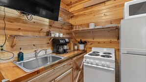 A wooden cabin kitchen with a sink, stove, and coffee maker. - Cedar Hollow Cabin: Cozy Black Hills Getaway (Rapid City)