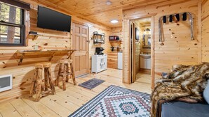 A wooden cabin interior with a dining area, kitchen, and bathroom. - Bison Trail House: Rustic Cabin Retreat (Rapid City)