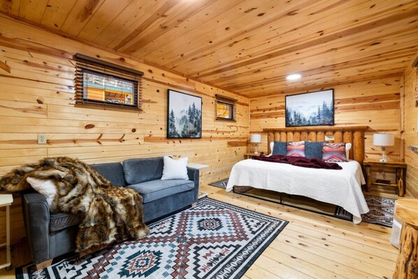 A cozy log cabin room with a bed, a couch, and a rug.