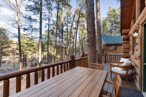 Una terraza de madera con una mesa y sillas, rodeada de altos pinos.