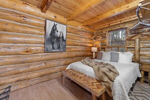 Un dormitorio de cabaña de madera con una cama, un banco, una lámpara y un cuadro de caballos.