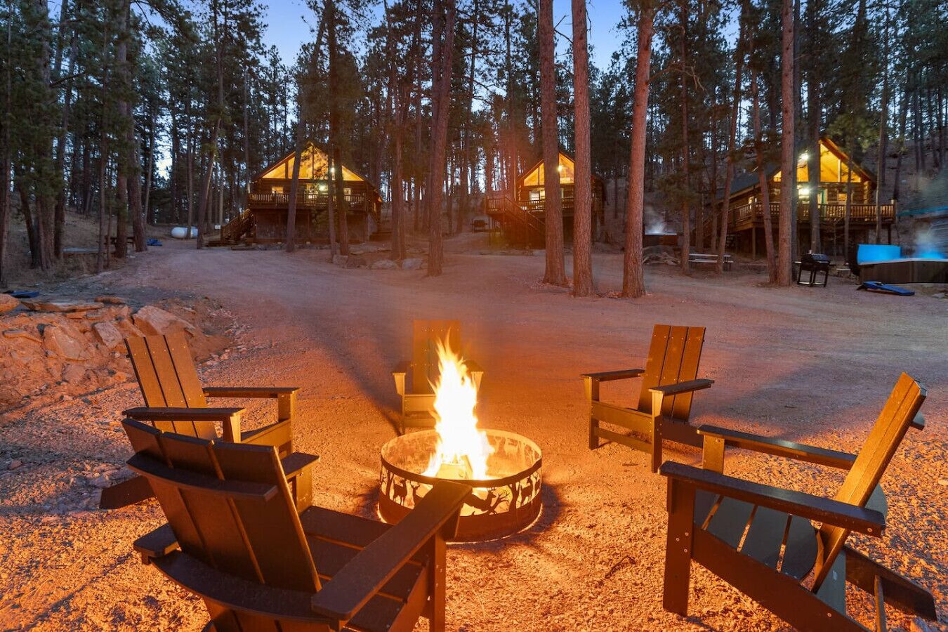 A cabin with a fire pit surrounded by Adirondack chairs in a forest setting.